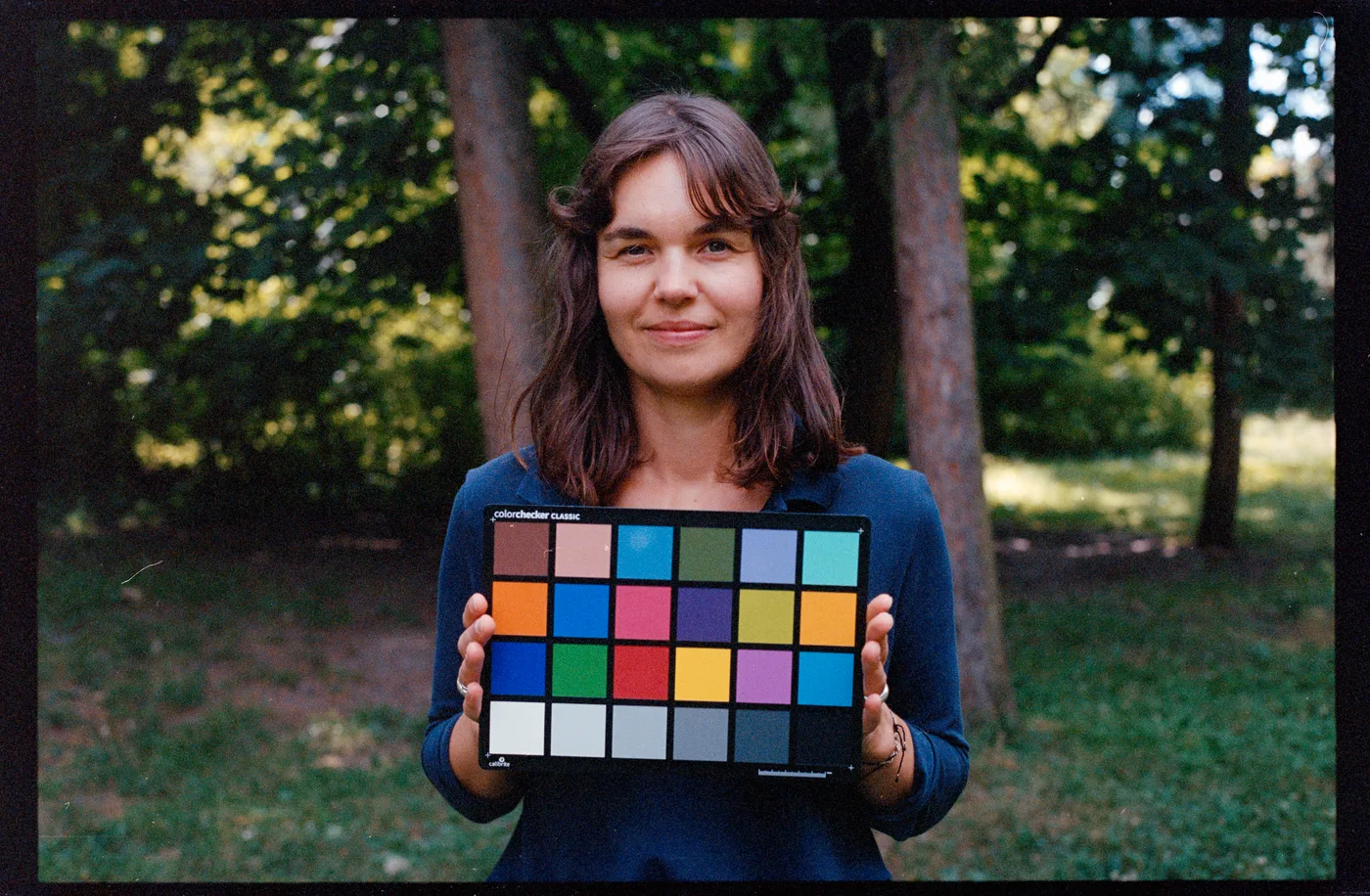 A woman holding a colour chart in front of her, trees and a lawn behind, on Portra 400, converted by Negative Lab Pro from a white-light raw.