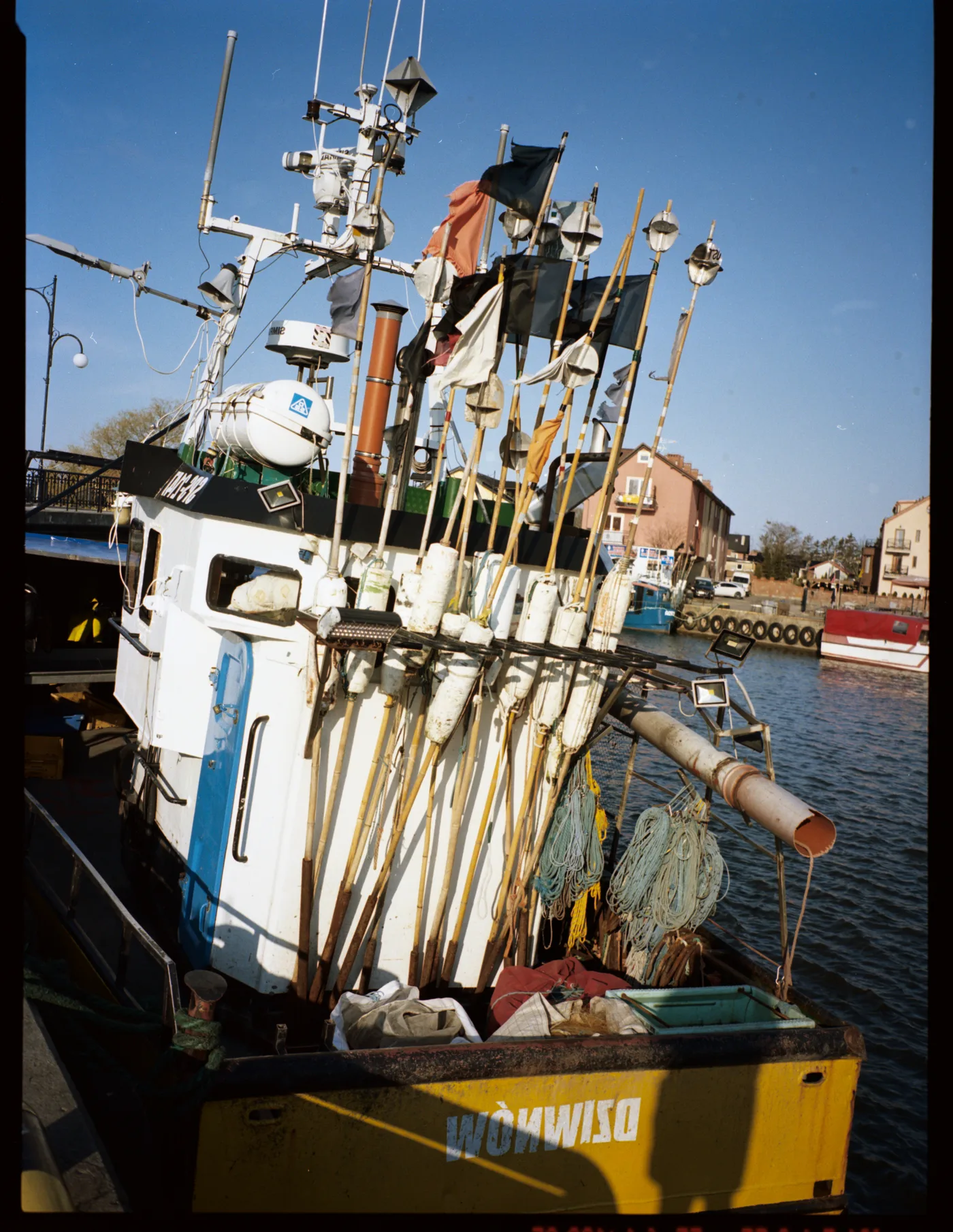 A fishing boat in harbour, its deck bristling with flagged buoy poles under a deep blue sky.